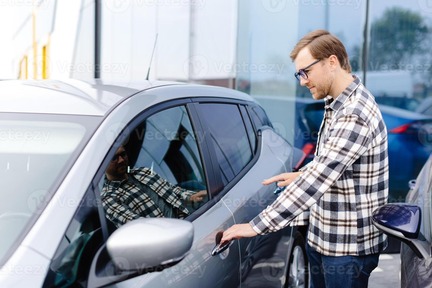 Young man buying auto at dealership salon and opening the door of his car. photo