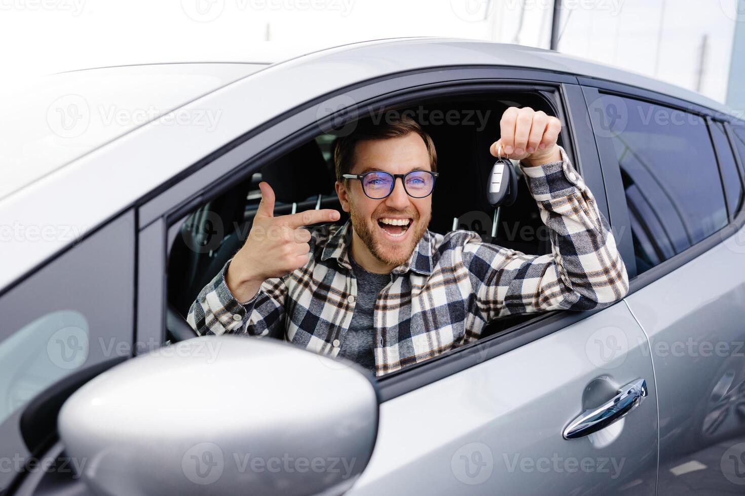 Excited man showing a car key, sitting inside his new vehicle. photo