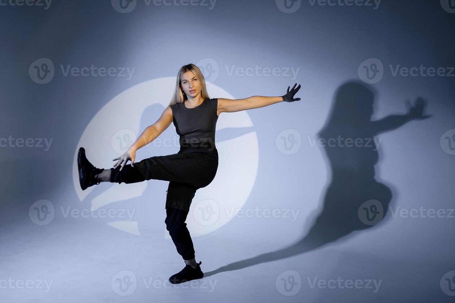 Young dancer performing modern dance illuminated by spotlight in studio. photo