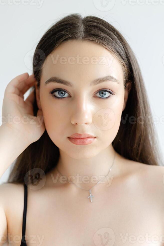 Young woman touching her hair wearing a necklace with a cross pendant. photo