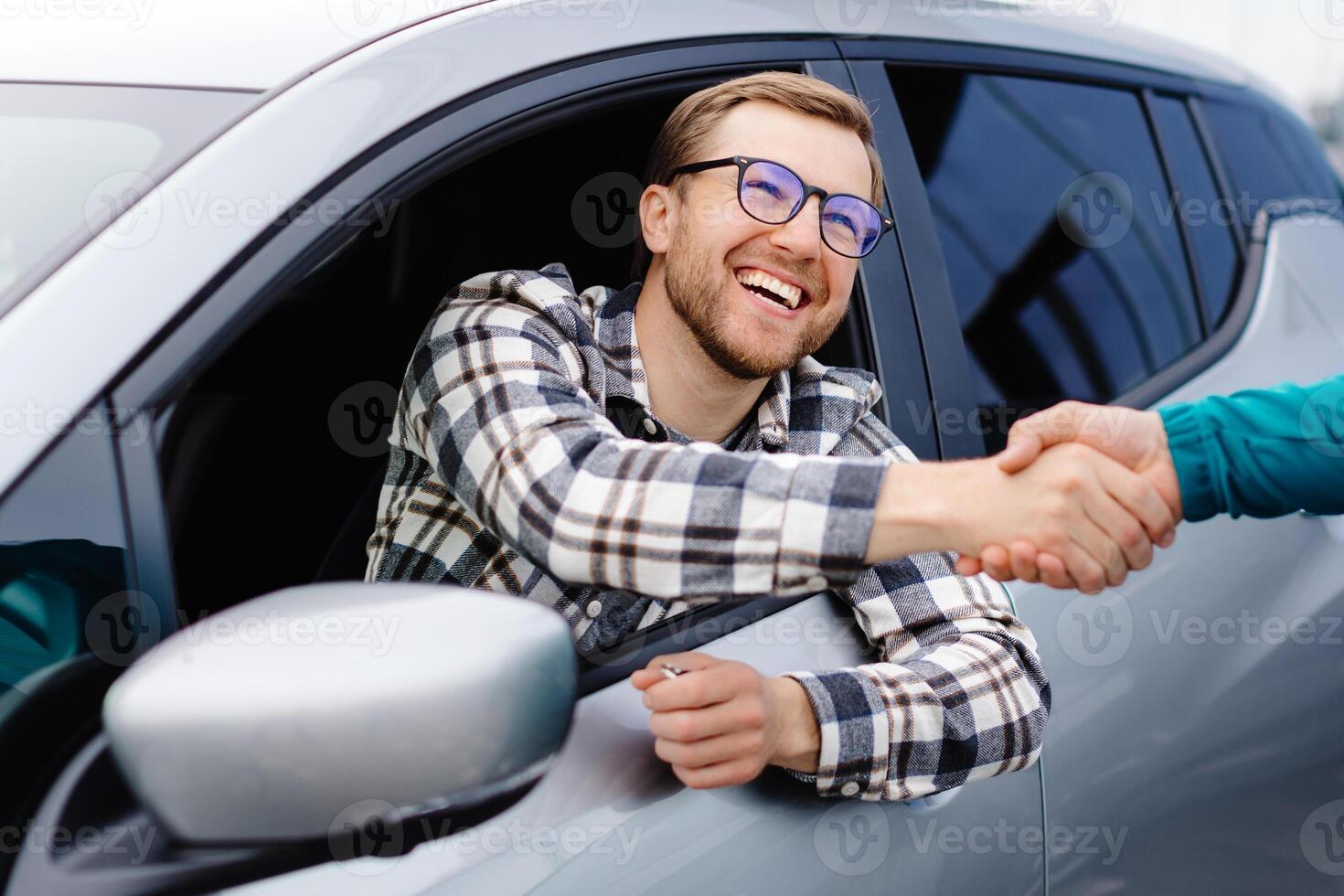 Man buying car and shaking hands with salesman against blurred auto, closeup. Concept of choosing and buying new car at showroom. photo