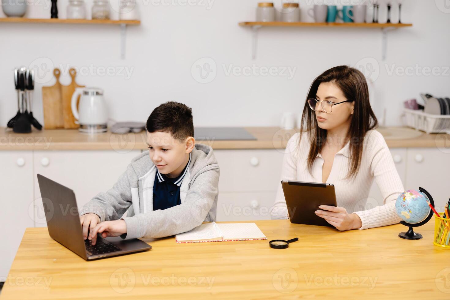 Young woman helps a boy with his lessons using a tablet and a globe. A homeschooling student does his homework with the help of a tutor. photo