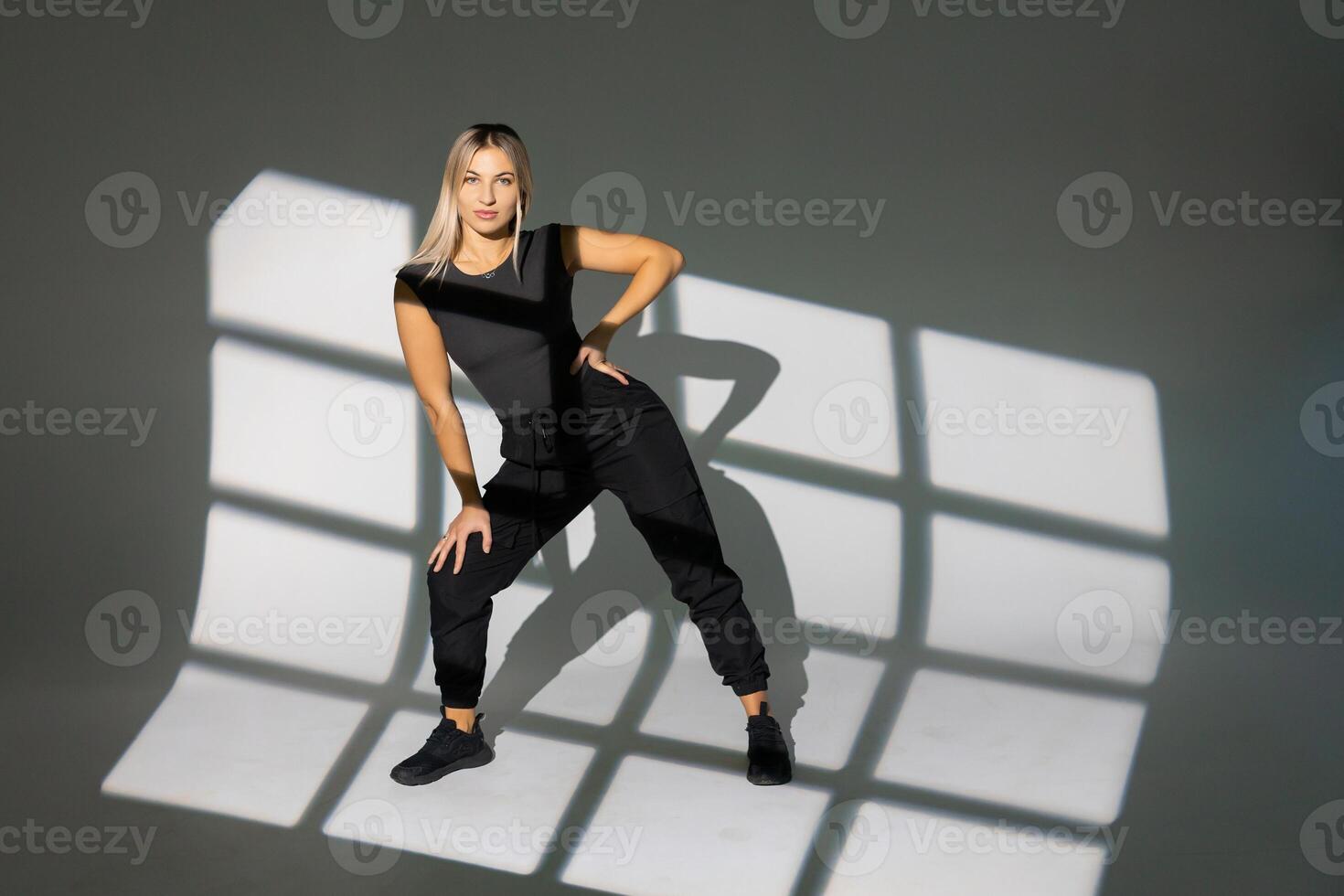 Dancer posing in studio with window light shadows, wearing black clothes. photo