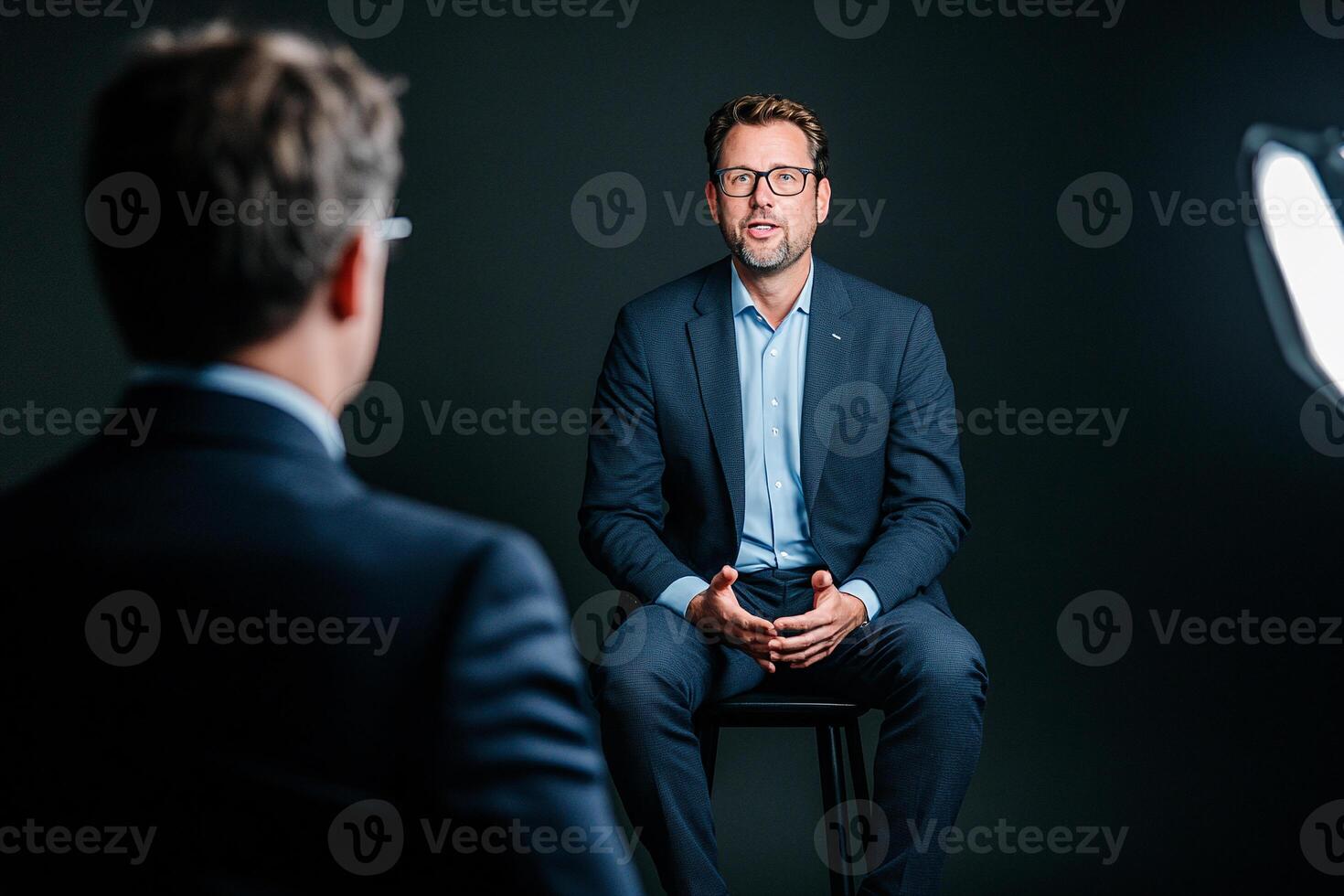 A man in a suit and tie sitting in front of a camera photo