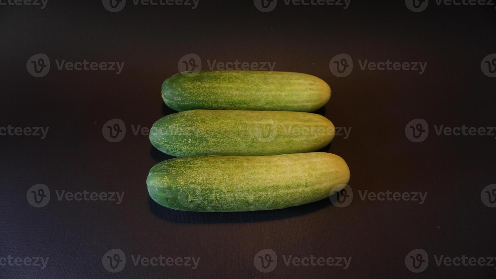 Three cucumbers are shown on a black surface photo