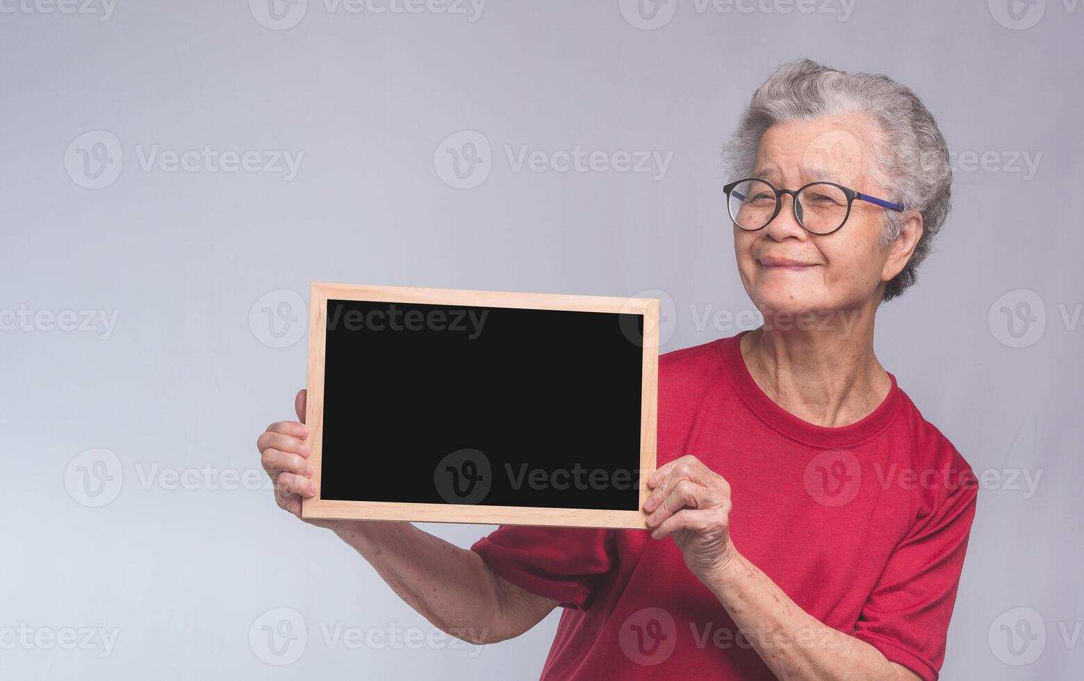 Senior woman holding a mini blackboard and looking at the camera with a smile while standing on a gray background. Space for text. photo