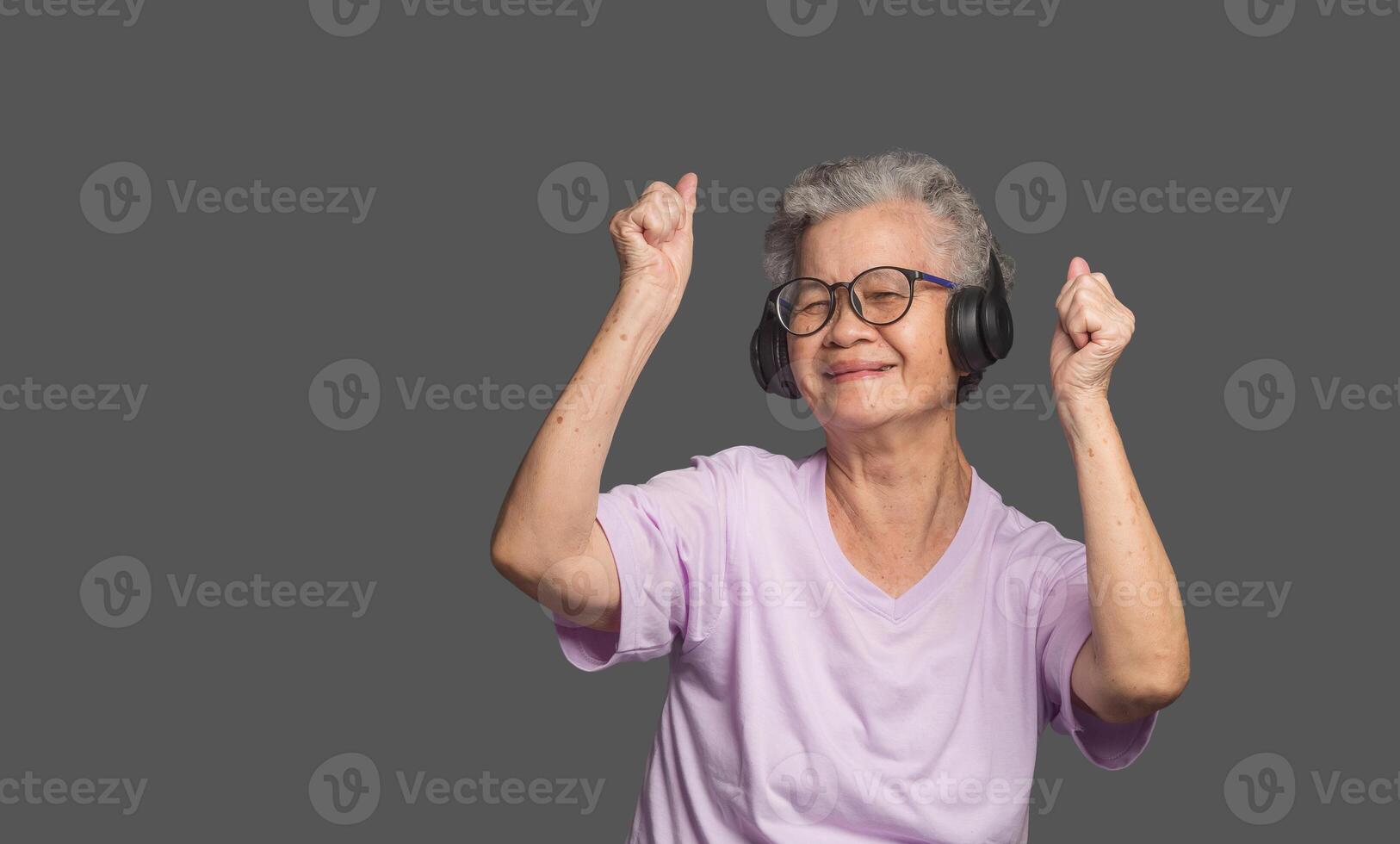 Senior Asian woman wearing wireless headphones with a smile while standing on a gray background photo
