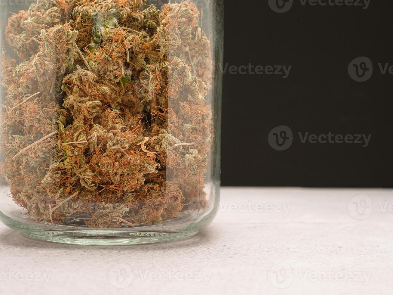 Dried cannabis buds flower in a jar glass on the table with a black background photo