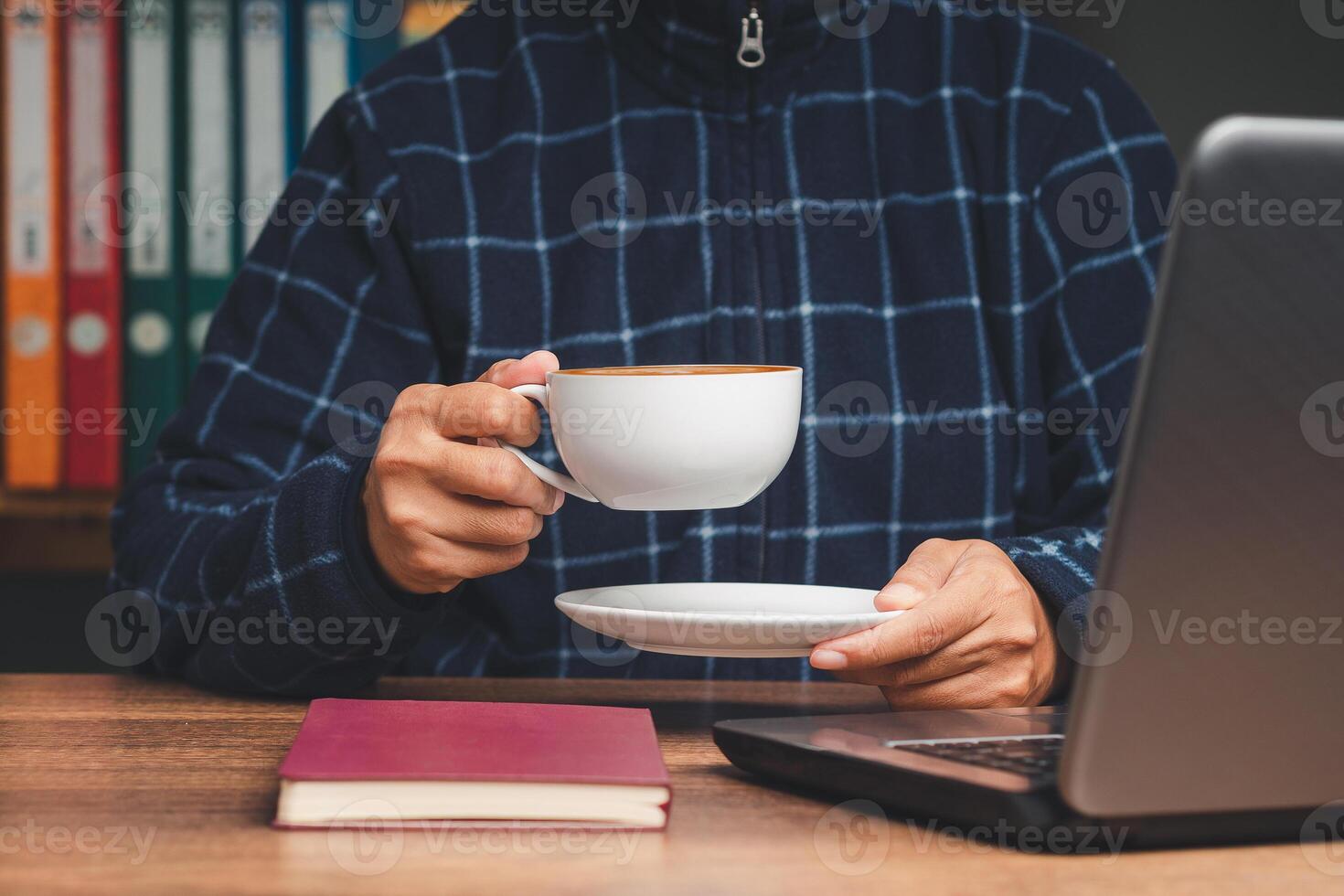 Businessman in a sweater hand holding a cup of coffee while sitting and working at the table. Close-up. photo