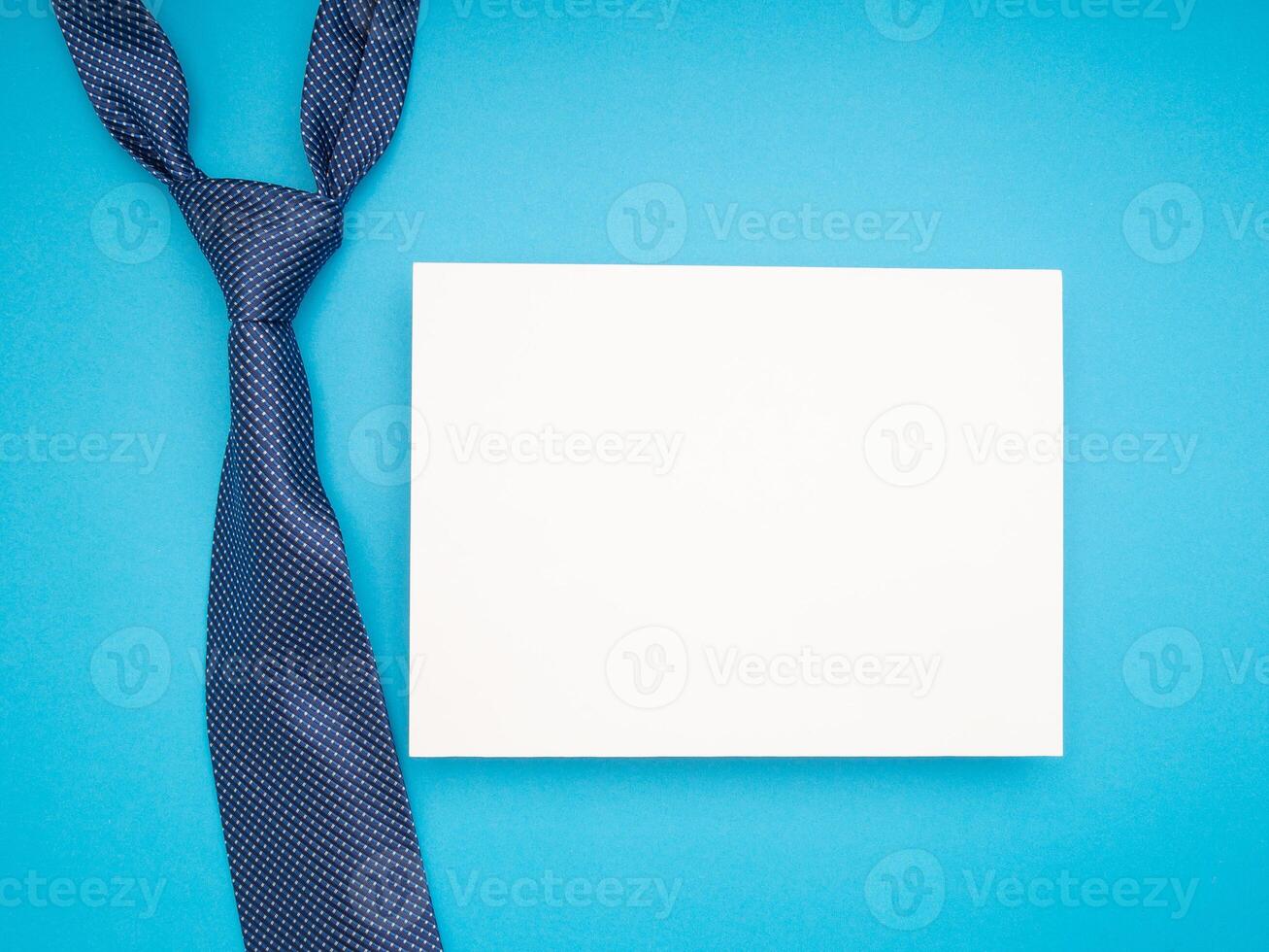 Top view of a necktie and a blank white paper over a blue background photo
