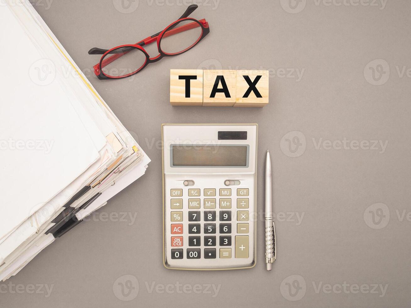 Stack of documents with binder clips, glasses, calculator, and Wooden cubes with the letters TAX on a gray background photo