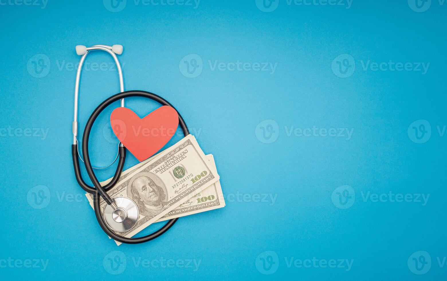 Top view of a stethoscope, US dollar banknotes, and a red heart symbol on a blue background photo