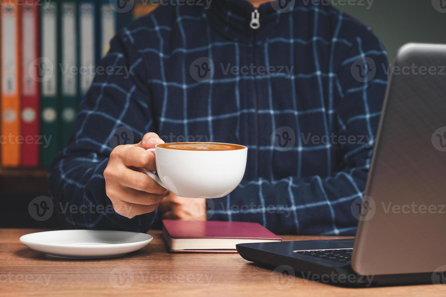 Businessman in a sweater hand holding a cup of coffee while sitting and working at the table photo