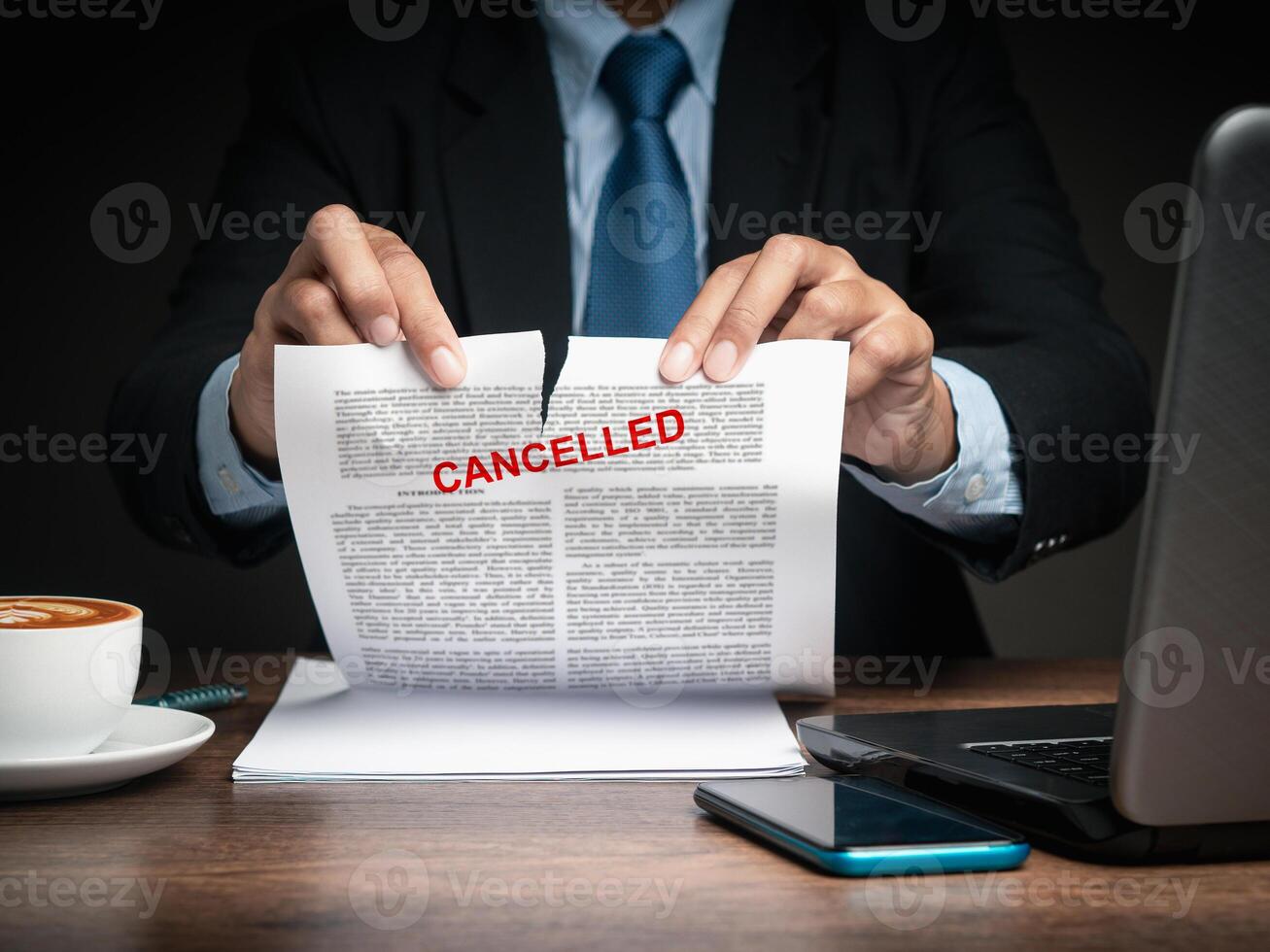 Businessman in a suit tearing up a canceled contract while sitting at the table photo