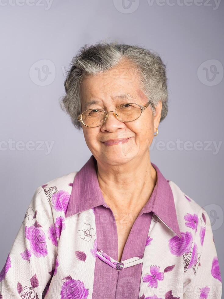 An elderly Asian woman looking at the camera with a smile while standing on a gray background. photo