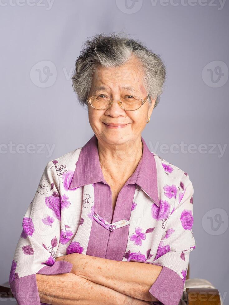Beautiful an elderly Asian woman looking at the camera with a smile while standing on a gray background photo