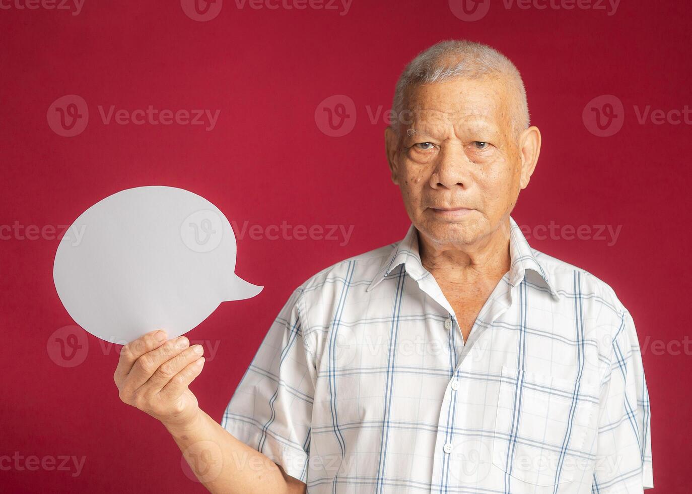 Senior man holding a blank speech bubble and looking at the camera while standing on a red background photo