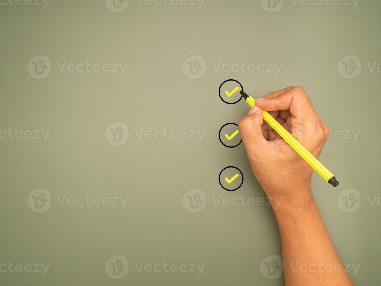 Hand holding a pen check-marking on the checklist box on a green background. Top view. photo