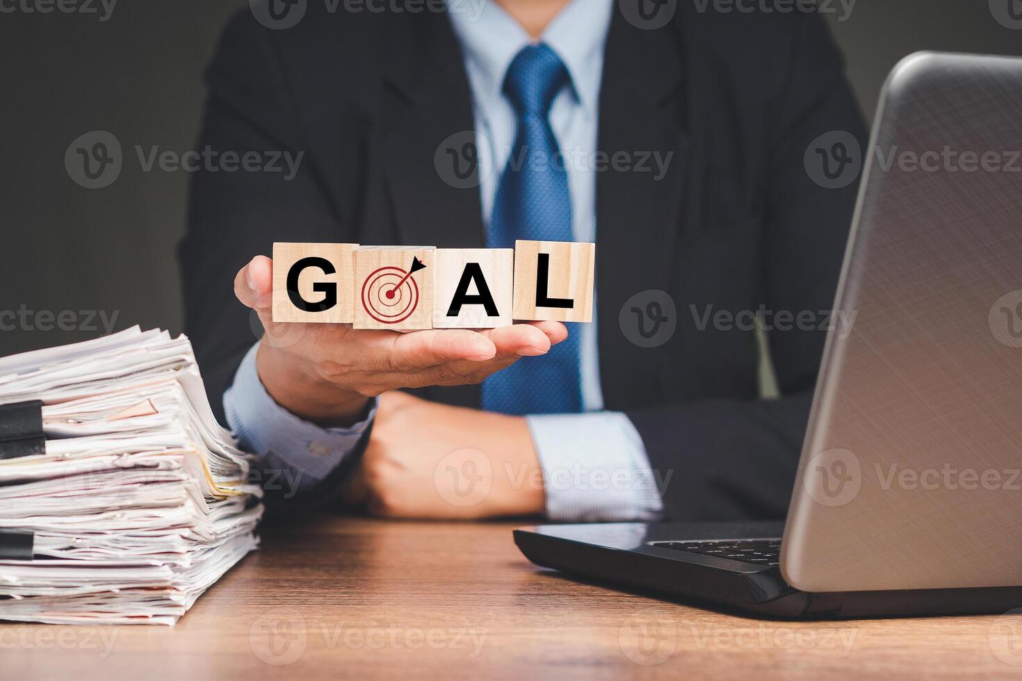Businessman holding wooden cubes with the letters GOAL and a dartboard icon while sitting at the table photo