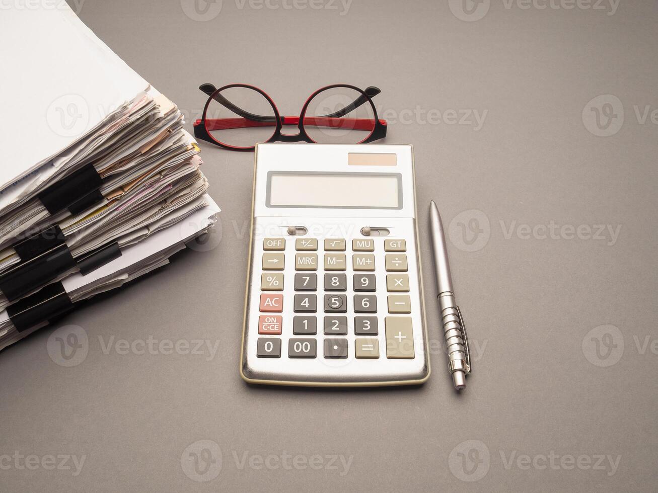 Stack of documents with binder clips, glasses, and calculator on a table photo