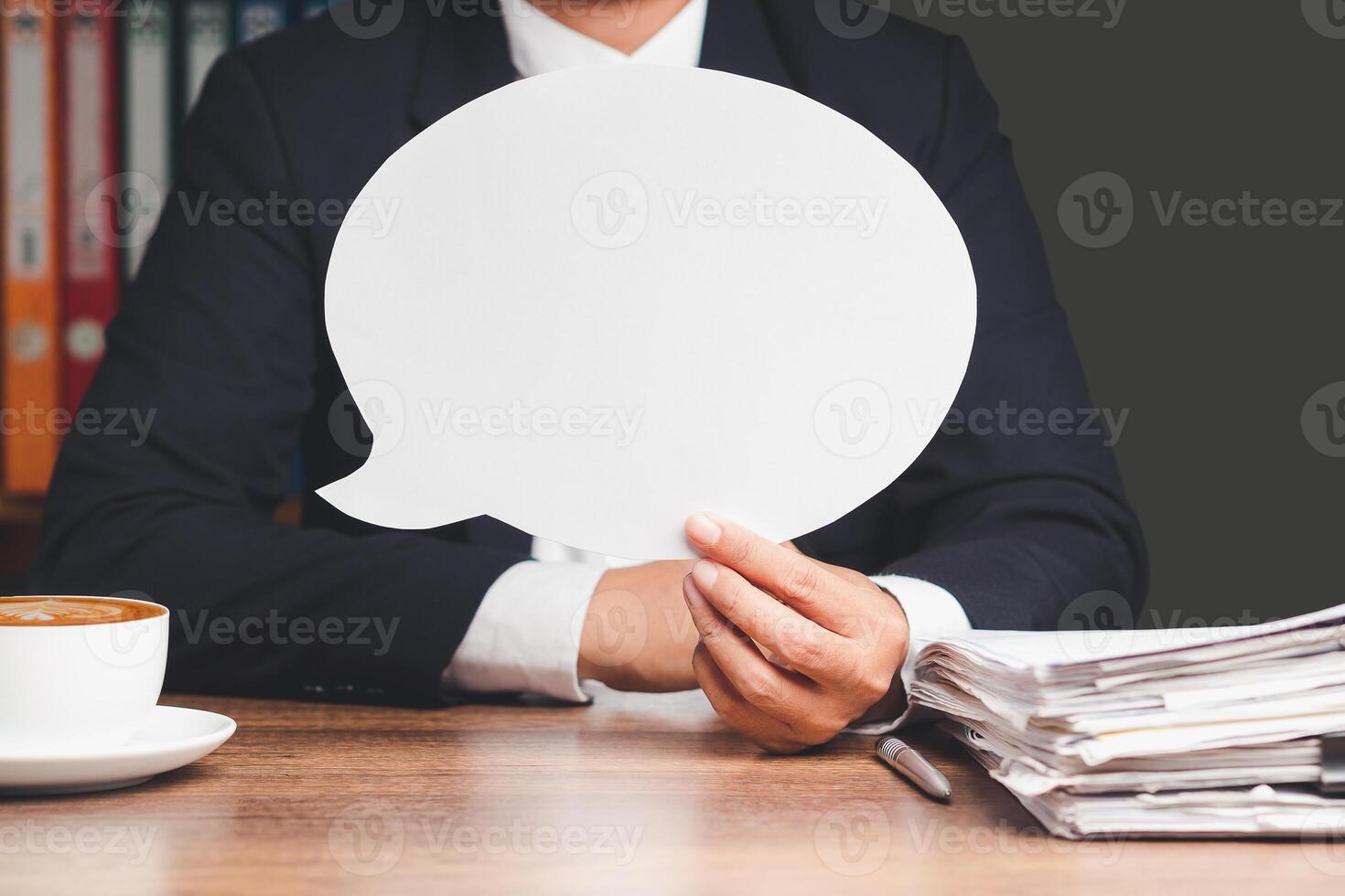 Businessman holding a blank white speech bubble while sitting at the table photo