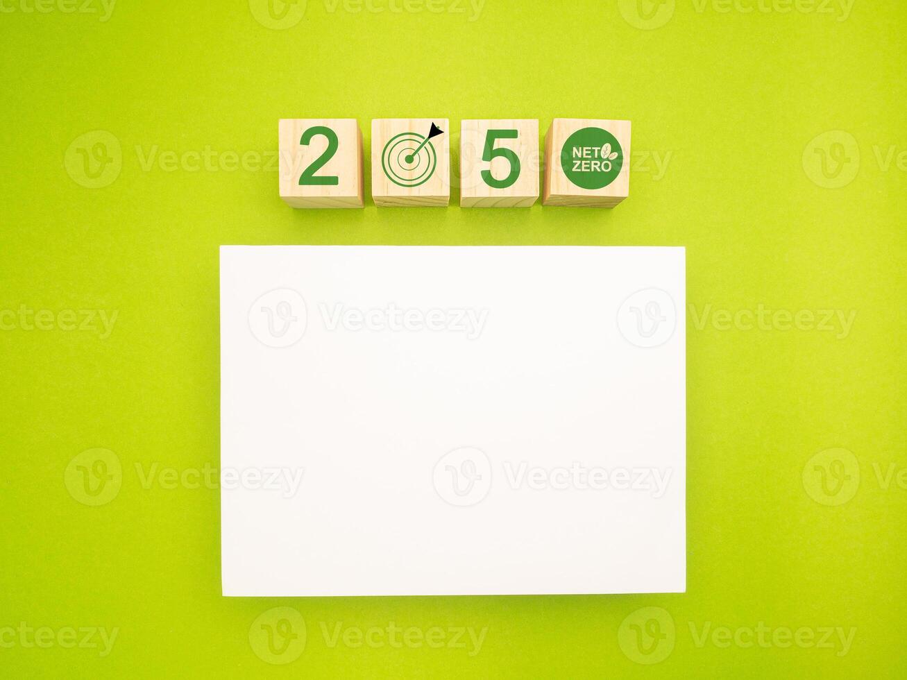 Wooden cubes with the letters 2050, graphic icons, and a blank white paper on a green background photo