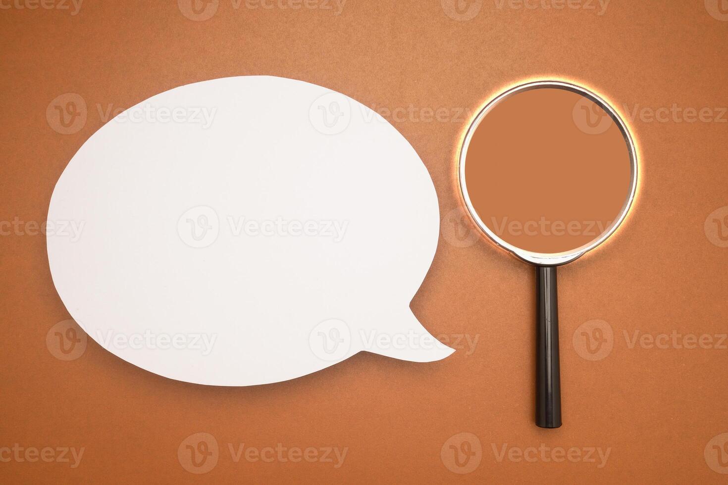 Top view of a blank white speech bubble and a magnifying glass isolated on a brown background photo