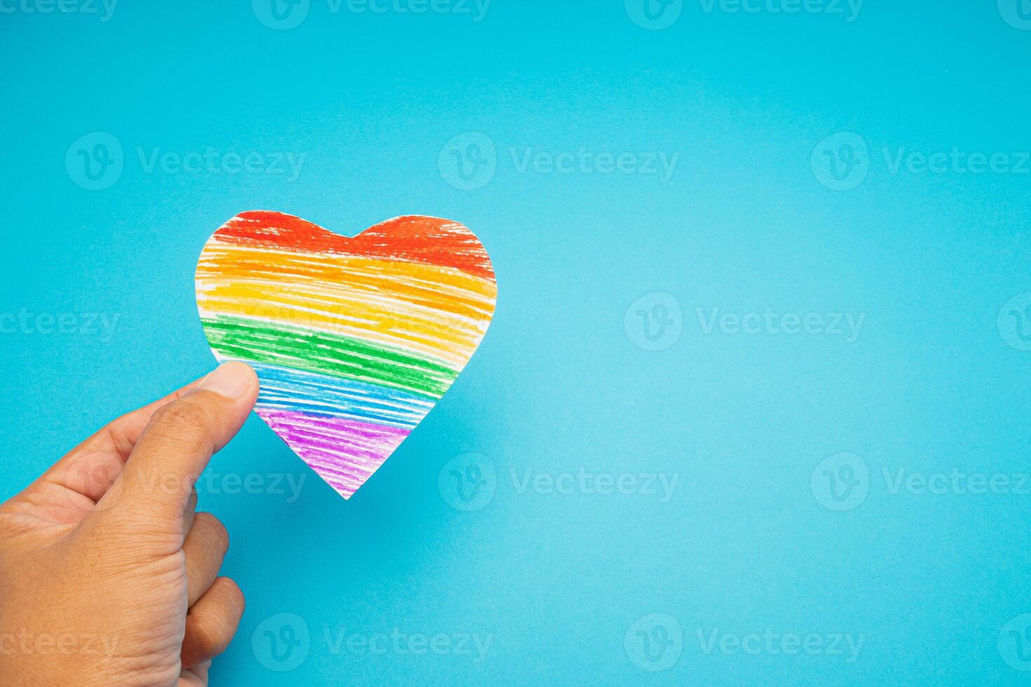 Hand holding a rainbow heart paper symbol on a blue background photo