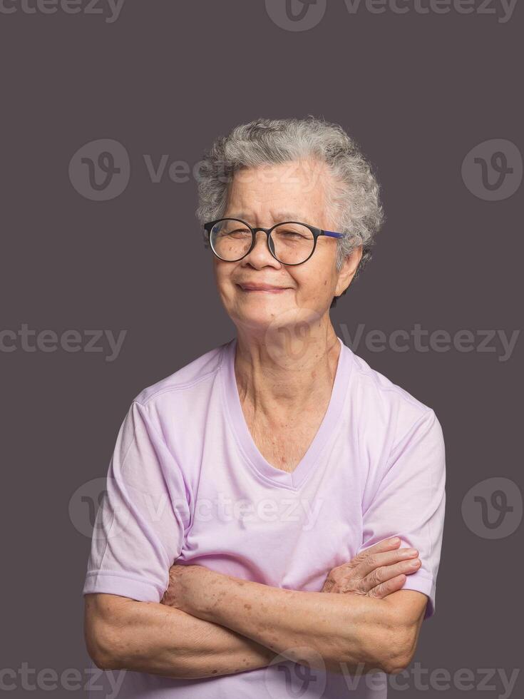 Beautiful elderly Asian woman looking at the camera with a smile while standing on a gray background. photo