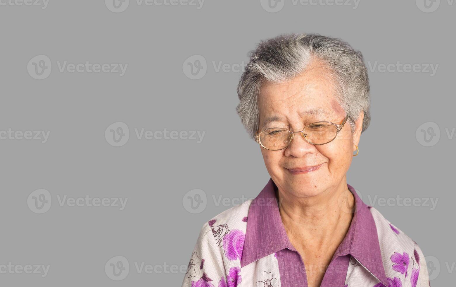 Beautiful elderly Asian woman looks down with a smile while standing on a gray background photo