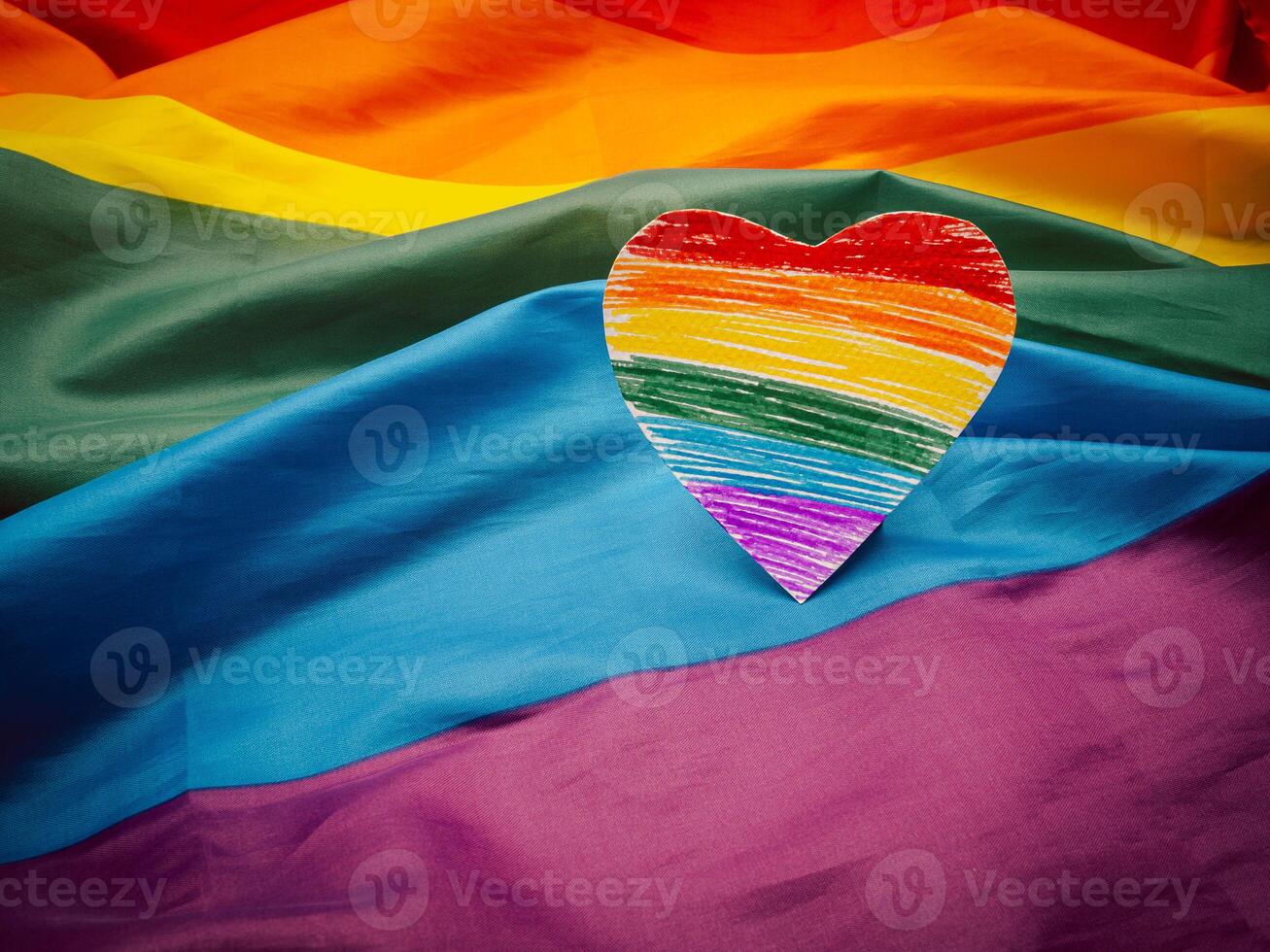 Top view of a rainbow heart shape symbol made from paper over the rainbow flag or LGBT flag. photo