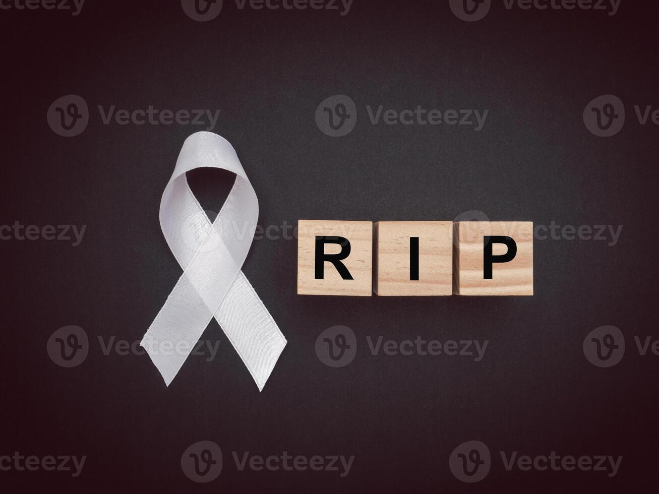 Top view of a white ribbon and wooden cubes with the letters RIP on a black background photo