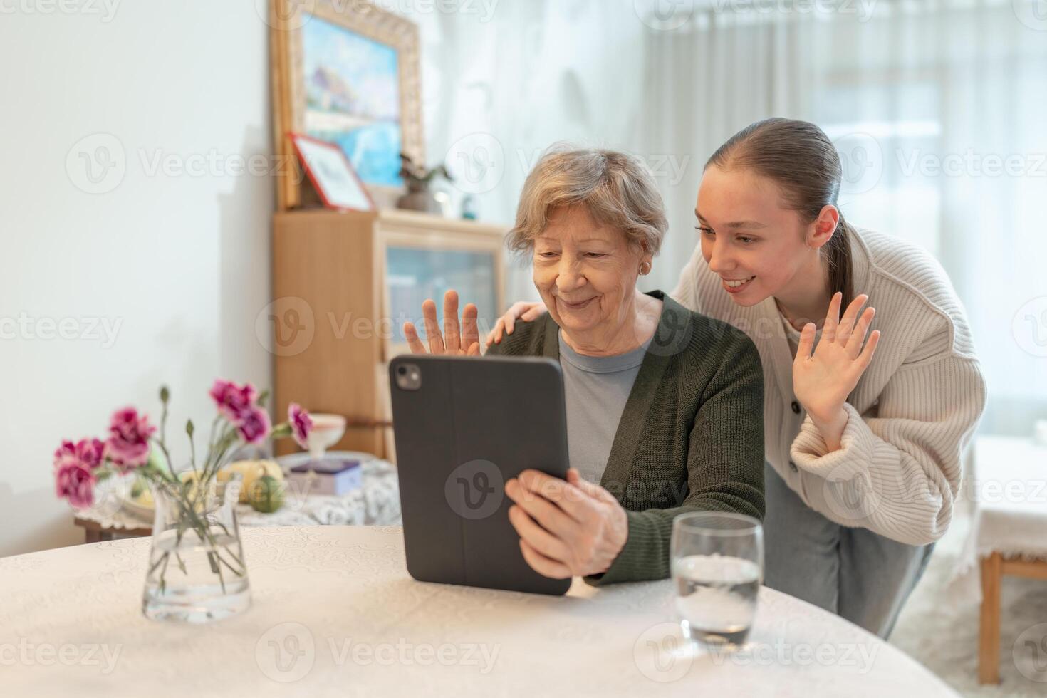 Elderly woman and young woman making a call with family on a tablet waving to the screen while sitting at home. Concept of technology and family connection. Seniors using digital technology. photo