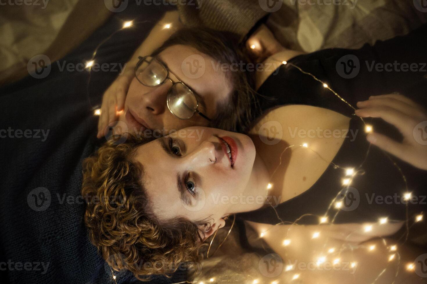 The couple lies on a soft blanket, head to head, the girl looks straight into the camera photo