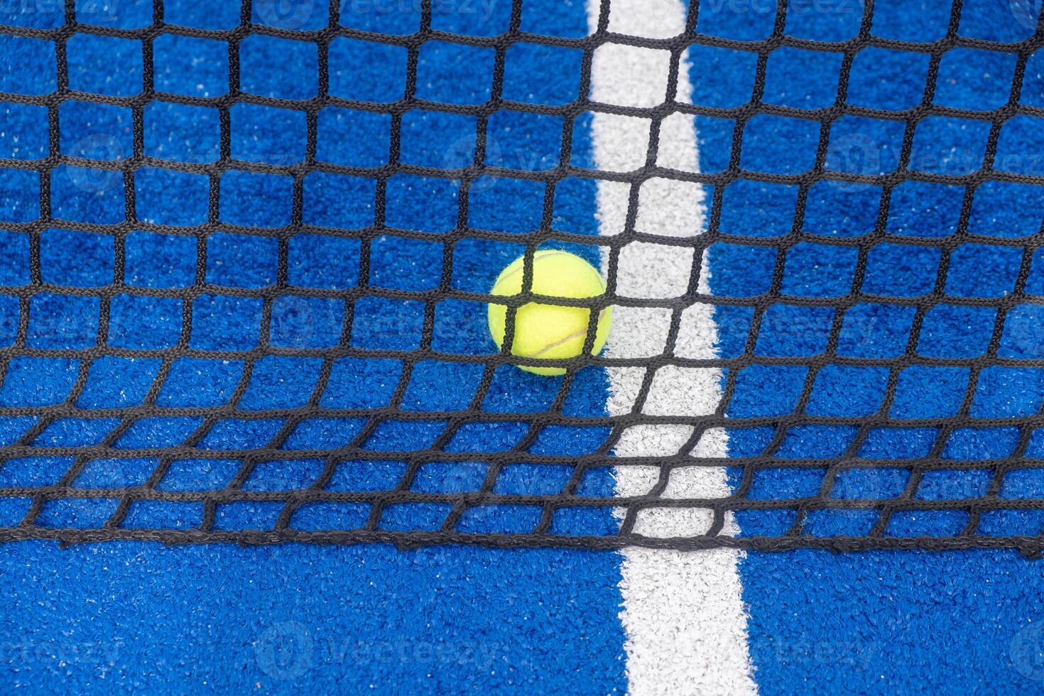 Tennis ball stuck in net on blue padel tennis court photo