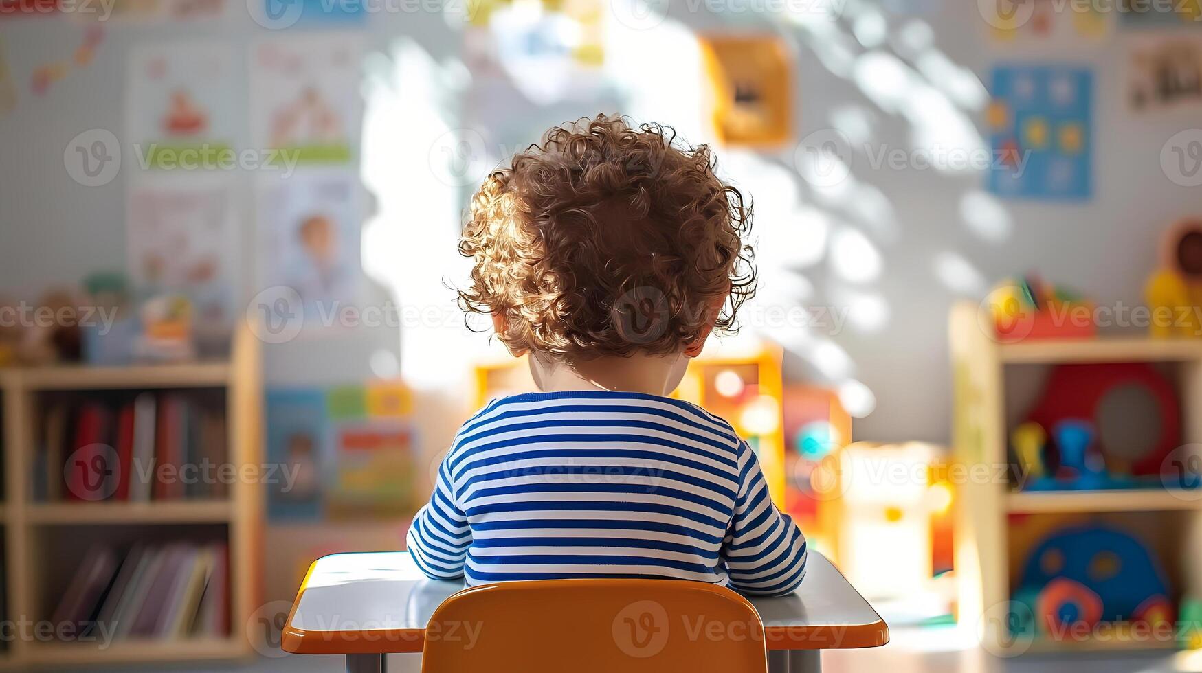 Toddler sitting at desk in playroom, observing toys and books photo