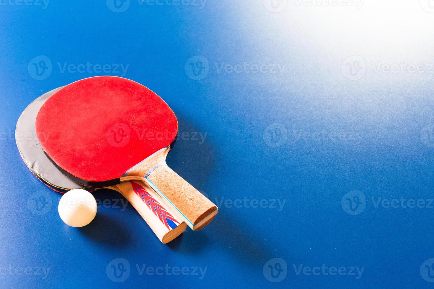 Two ping pong rackets and ball on blue table photo