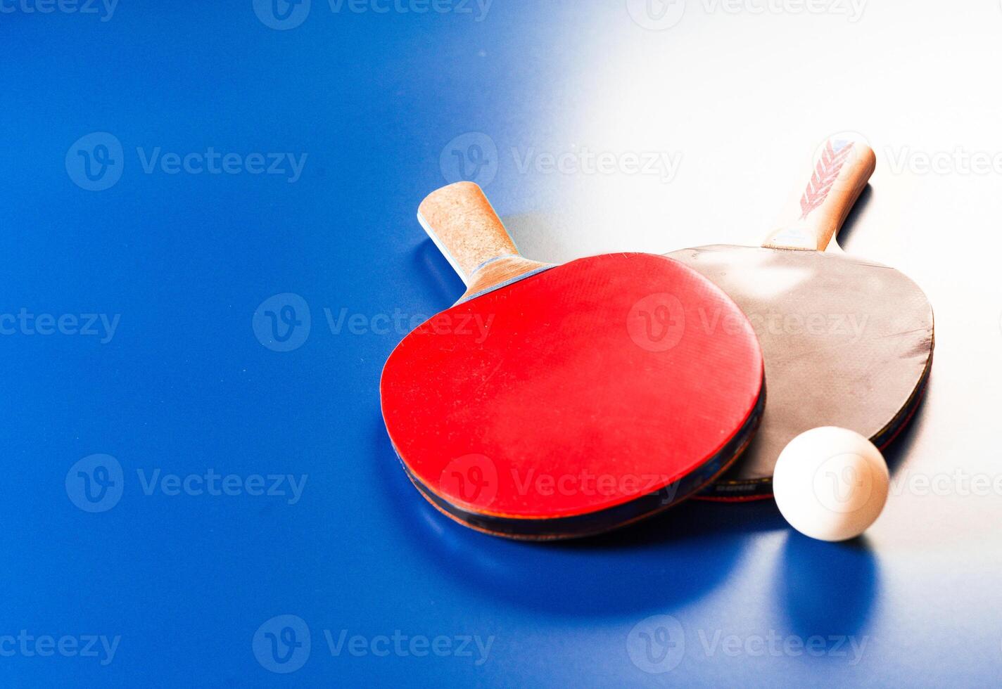 Two ping pong rackets and ball on blue table photo