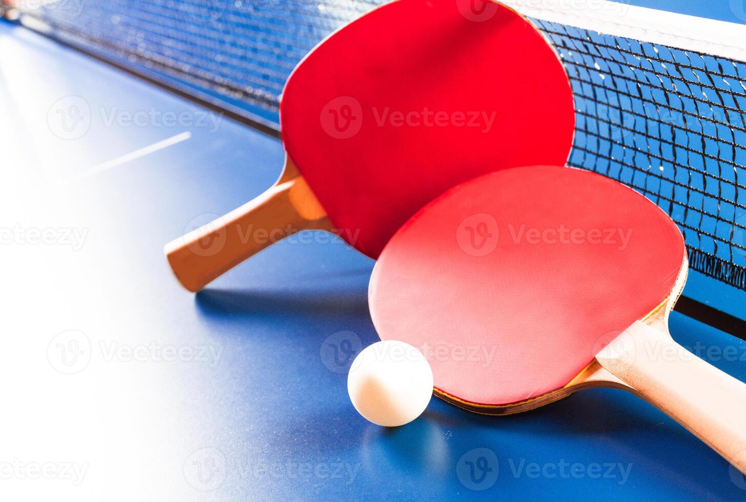 Two ping pong rackets and ball on blue table photo