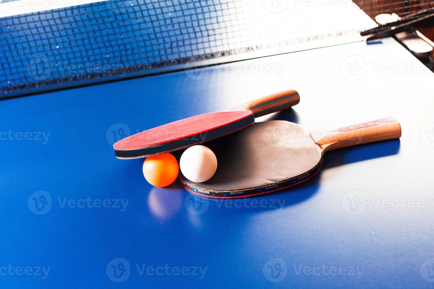 Two ping pong rackets and ball on blue table photo