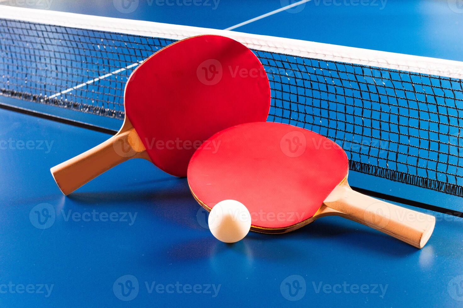 Two ping pong rackets and ball on blue table photo