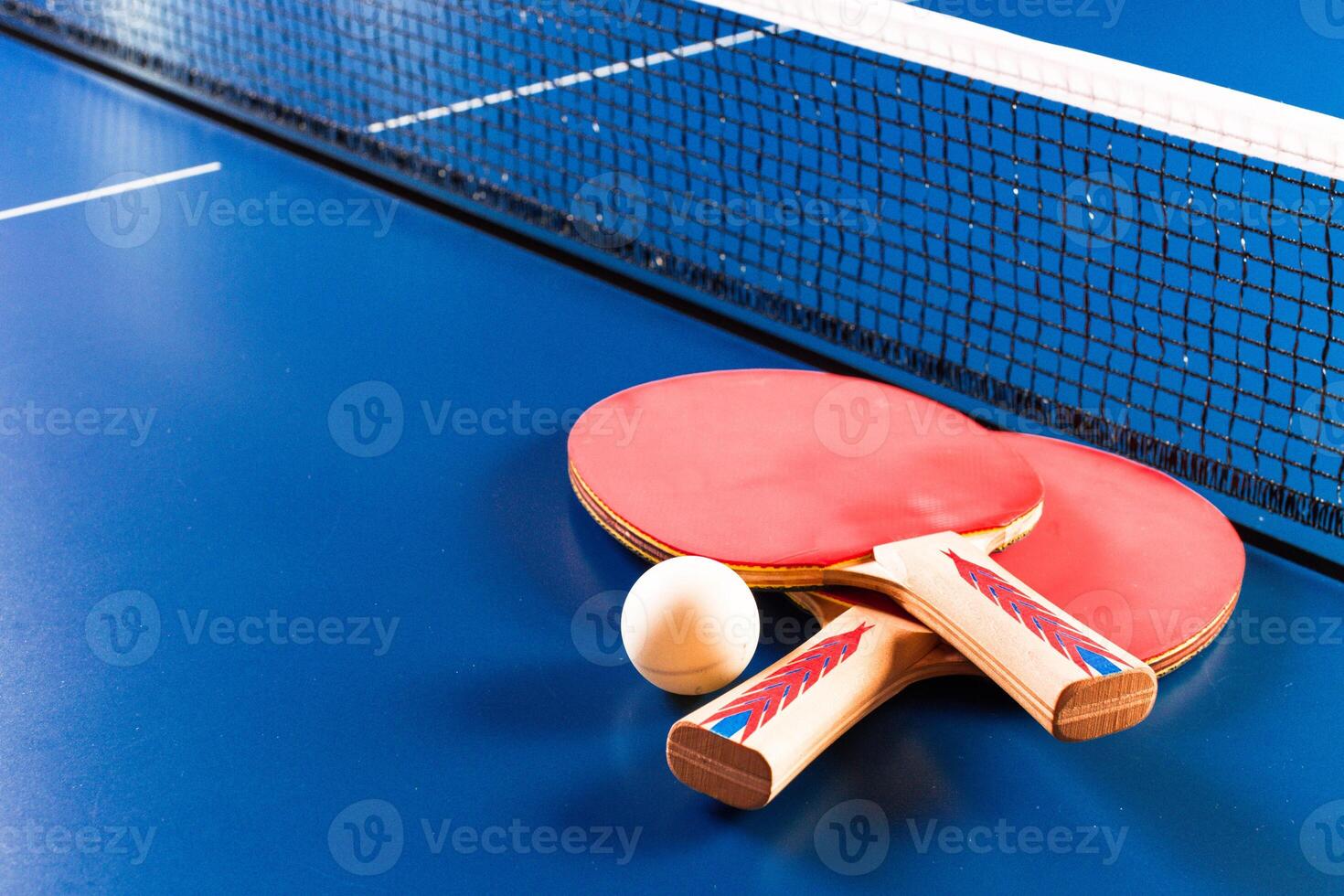 Two ping pong rackets and ball on blue table photo