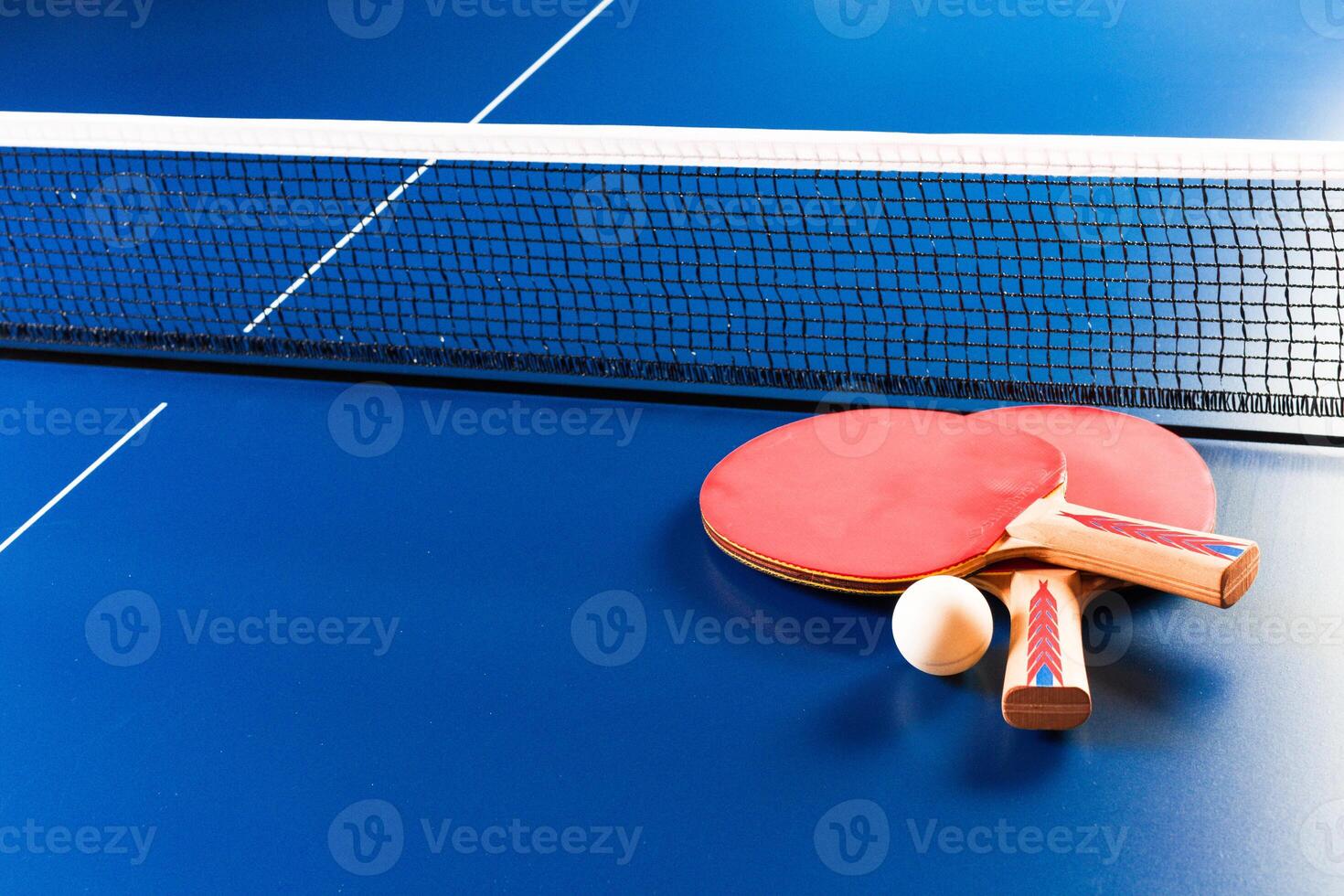 Two ping pong rackets and ball on blue table photo