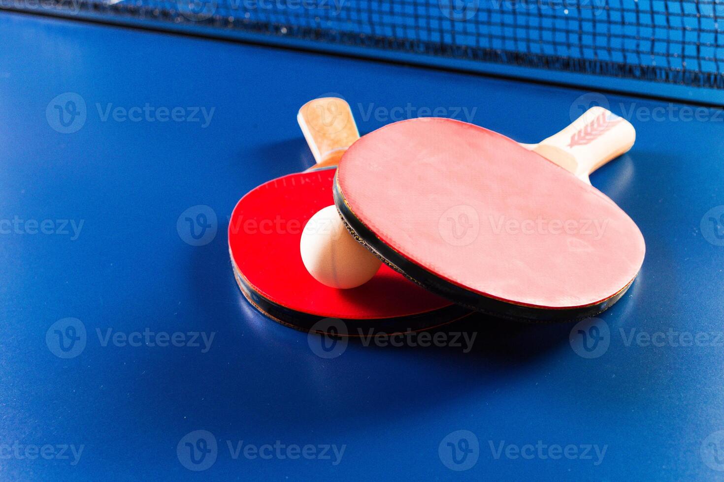 Two ping pong rackets and ball on blue table photo