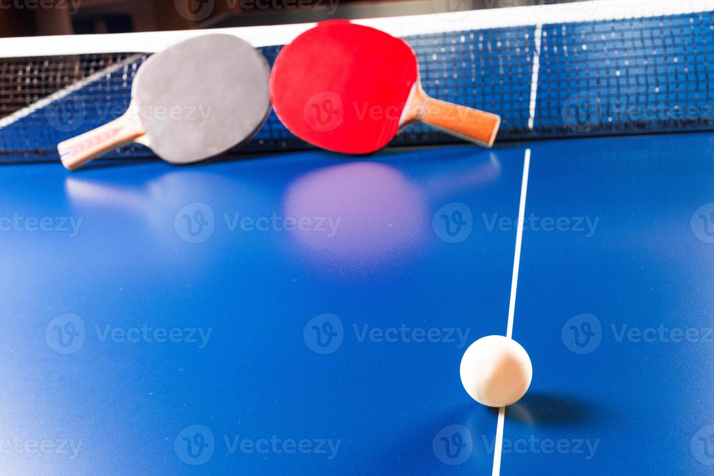 Two ping pong rackets and ball on blue table photo