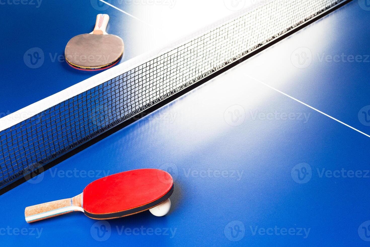 Two ping pong rackets and ball on blue table photo