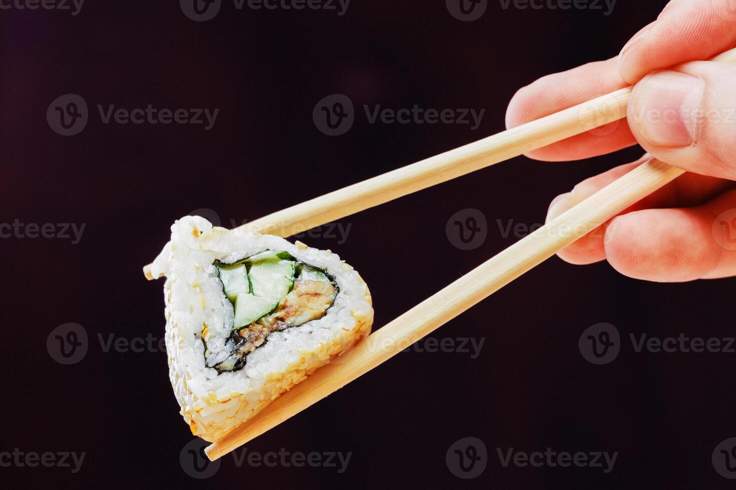 Hand holding sushi roll with chopsticks against dark background in a minimalist setting photo