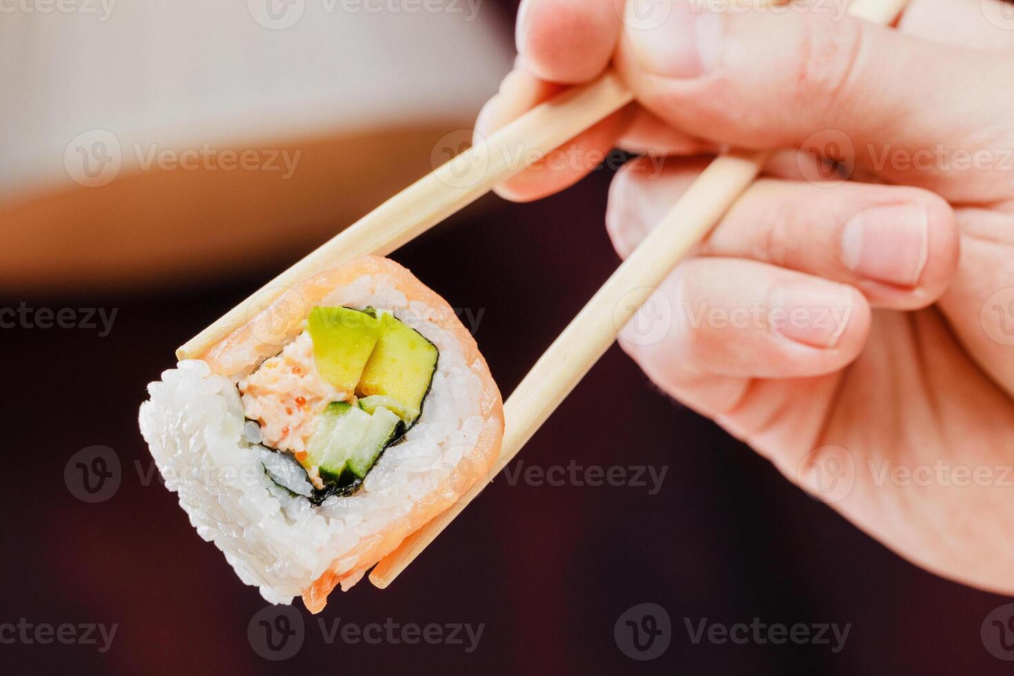 Enjoying fresh sushi roll with salmon and cucumber held by chopsticks in a cozy setting photo