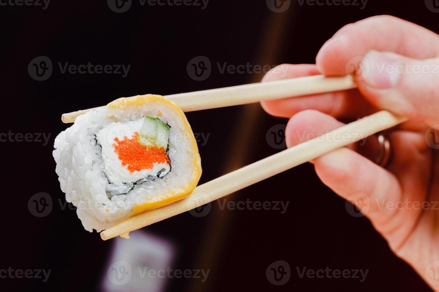 Delicious sushi roll being held with chopsticks in a cozy dining setting photo