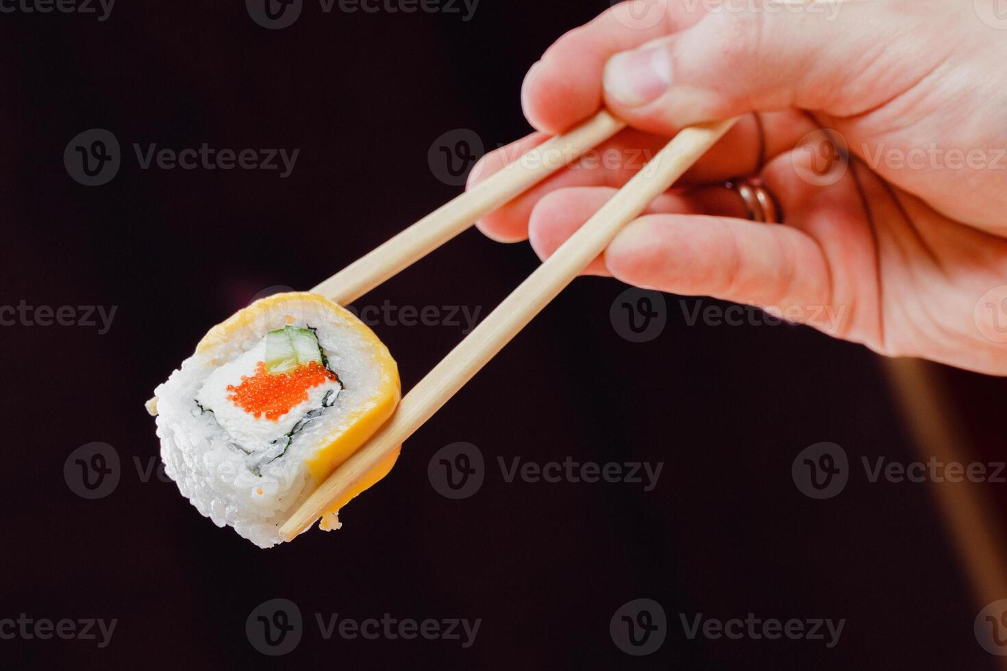 Hand holding sushi roll with chopsticks against dark background in a culinary setting photo
